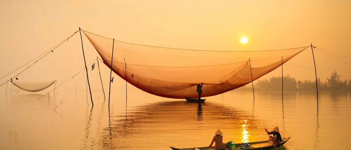 Two local people fishing from a canoe at sunset Hoian Vietnam
