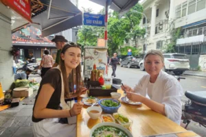Tourists eating traditional Vietnamese pho at a street food restaurant in Hanoi Old Quarter